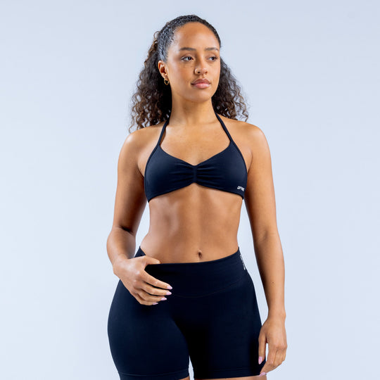 Dark strappy sports bra with center knot, thin straps, logo label on right.