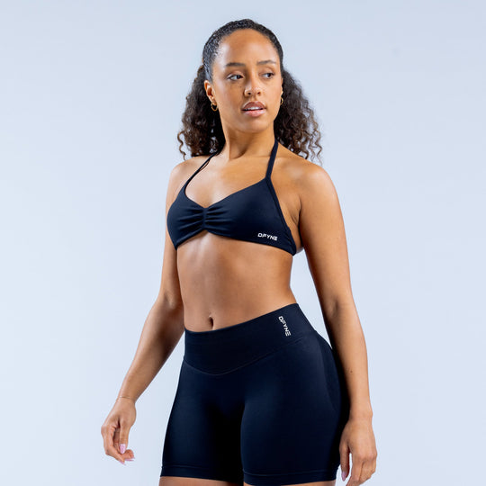 Dark strappy sports bra with ruched knot center and thin adjustable straps.