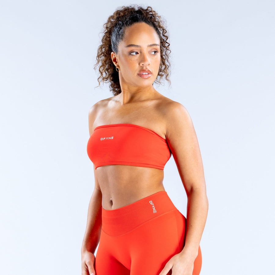 Red bandeau sports bra with off-shoulder neckline, wide band, and front logo.