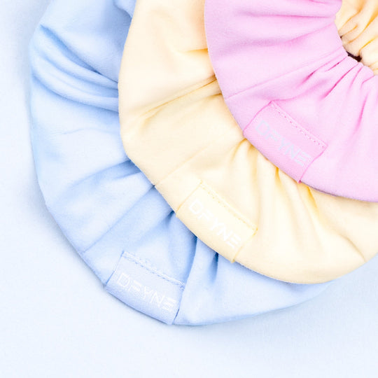 Scrunchie close-up in pink and cream fabric, stitched logo detail on gathered band