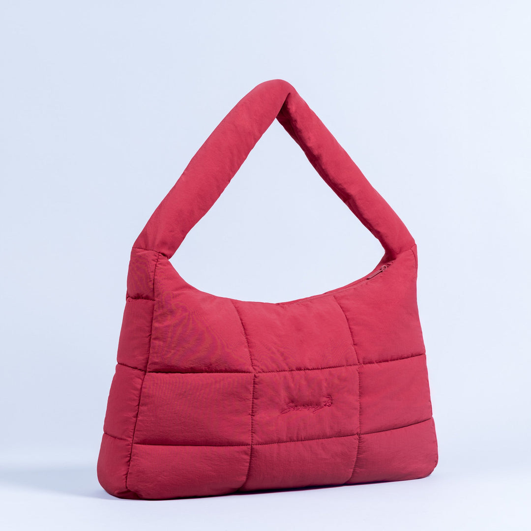Red quilted puffer bag with top handle and rounded hobo shape.