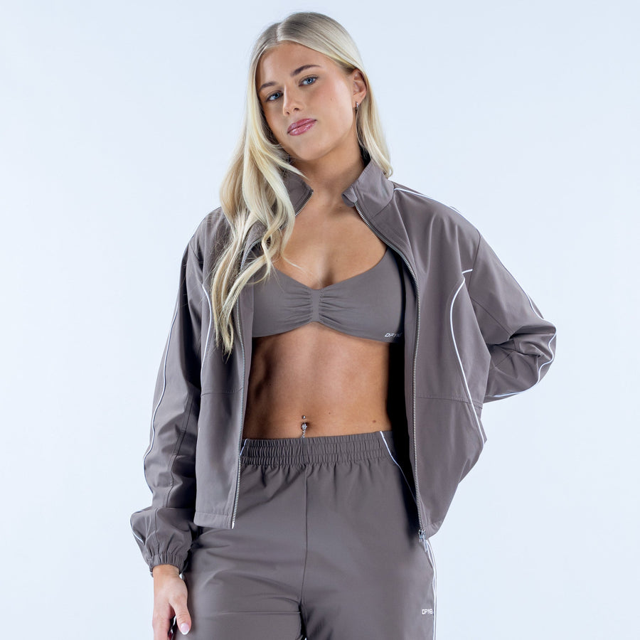 Women's gray track jacket worn over sports bra, full-zip with white piping